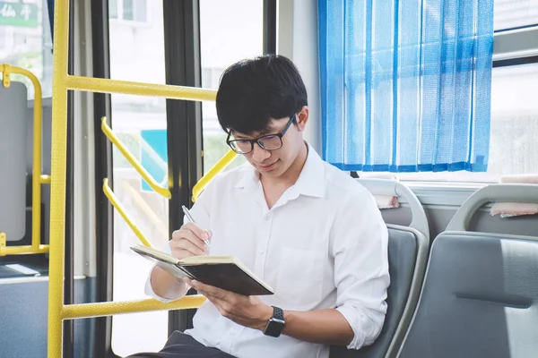 Jovem asiático viajante sentado em um ônibus e ler livro ou pr — Fotografia de Stock