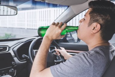 Genç Asyalı adam sarhoş bira şişesi ile bir araba kullanıyor 