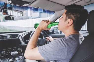 Genç Asyalı adam sarhoş bira şişesi ile bir araba kullanıyor 