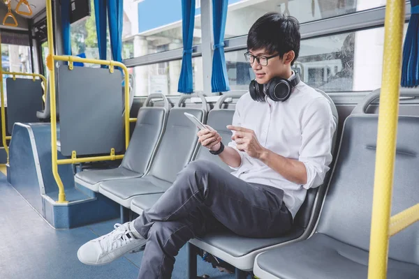 Fiatal ázsiai férfi utas ül a buszon használ smartphone néz — Stock Fotó