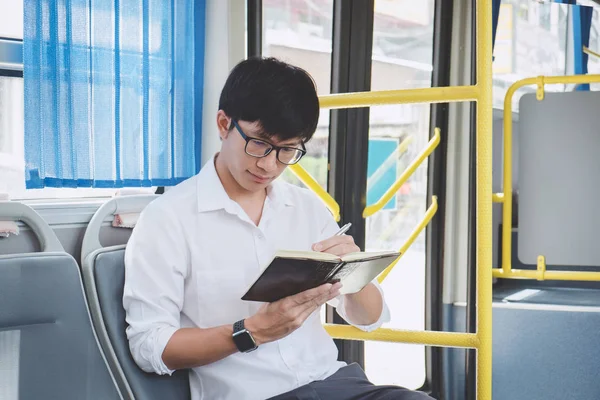 Young Asian man traveler sitting on a bus and reading book or pr