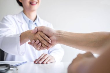 Professional female doctor in white coat shaking hand with patie clipart