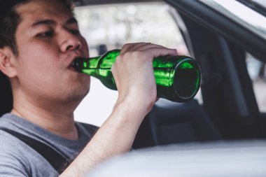 Young asian man drives a car with drunk a bottle of beer behind  clipart