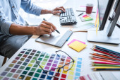Bild eines männlichen kreativen Grafikdesigners, der an der Farbauswahl arbeitet und am Arbeitsplatz mit Werkzeugen und Zubehör auf einem Grafik-Tablet zeichnet.