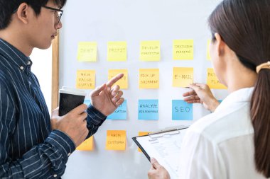 İki yaratıcı iş adamı toplantı ve planlama fikri paylaşmak için beyaz tahtaya yapışkan notlar, analiz veri grafikleri ve takım çalışması stratejisi beyin fırtınası ile grafik kullanırlar.