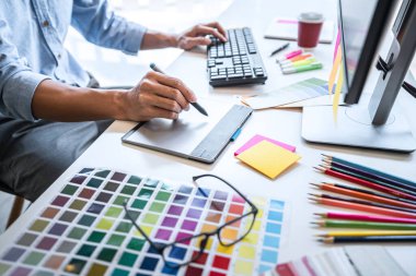 Image of male creative graphic designer working on color selection and drawing on graphics tablet at workplace with work tools and accessories in workspace. clipart
