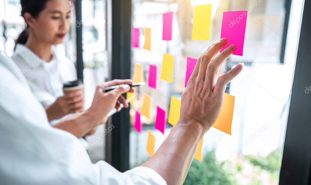 Young creative team professional using post it notes in glass wall to writing strategy business plan to development grow to success.