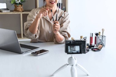 Mutlu gülümseyen zarif kadın ya da video kaydında fırçasıyla güzellik blogcusu. İnceleme ürünü kamera ekranında video blogları hakkında özel ders hazırlıyor..