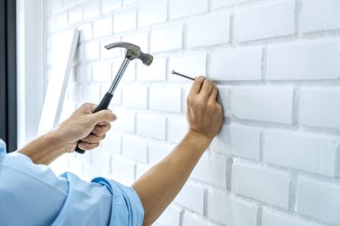 Tuğla duvara çivi çakmak için çekiç ve iç tasarım konseptini kullanarak evdeki tadilatı yapan bir zanaatkar..