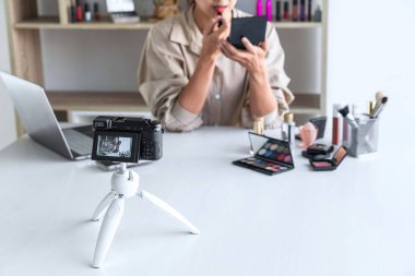 Mutlu gülümseyen zarif kadın blogcu, makyaj malzemesi kozmetik inceleme ürünü sunuyor ve kamera ekranında sosyal ağa canlı yayın yapan video bloglarını öğretiyor..