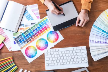 İş yerinde iş araçları ve aksesuarlarıyla renk seçimi ve grafik tableti üzerinde çalışan kadın yaratıcı grafik tasarımcı resmi.