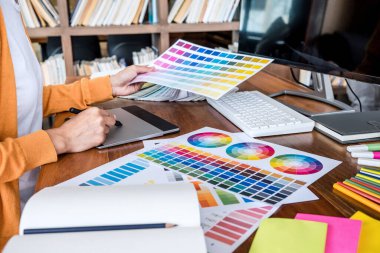 İş yerinde iş araçları ve aksesuarlarıyla renk seçimi ve grafik tableti üzerinde çalışan kadın yaratıcı grafik tasarımcı resmi.