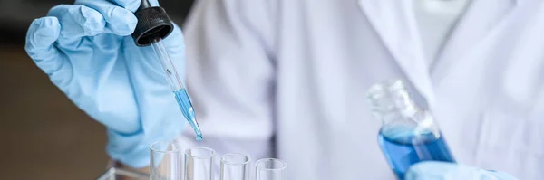 Biochemistry laboratory research, Scientist or medical in lab coat holding test tube with Using Microscope reagent with drop of color liquid over glass equipment working at the laboratory.