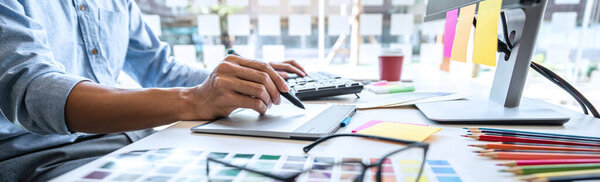 Image of male creative graphic designer working on color selection and drawing on graphics tablet at workplace with work tools and accessories in workspace.