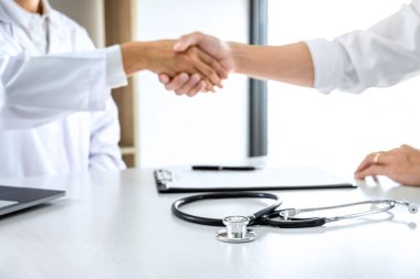 Tıp ve sağlık konsepti, beyaz önlüklü profesyonel erkek doktor başarılı tedavi yöntemleri önerdikten sonra hastayla tokalaşıyor.