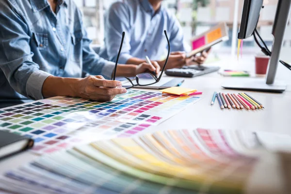 Two colleague creative graphic designer working on color selection and color swatches, drawing on graphics tablet at workplace with work tools and accessories.