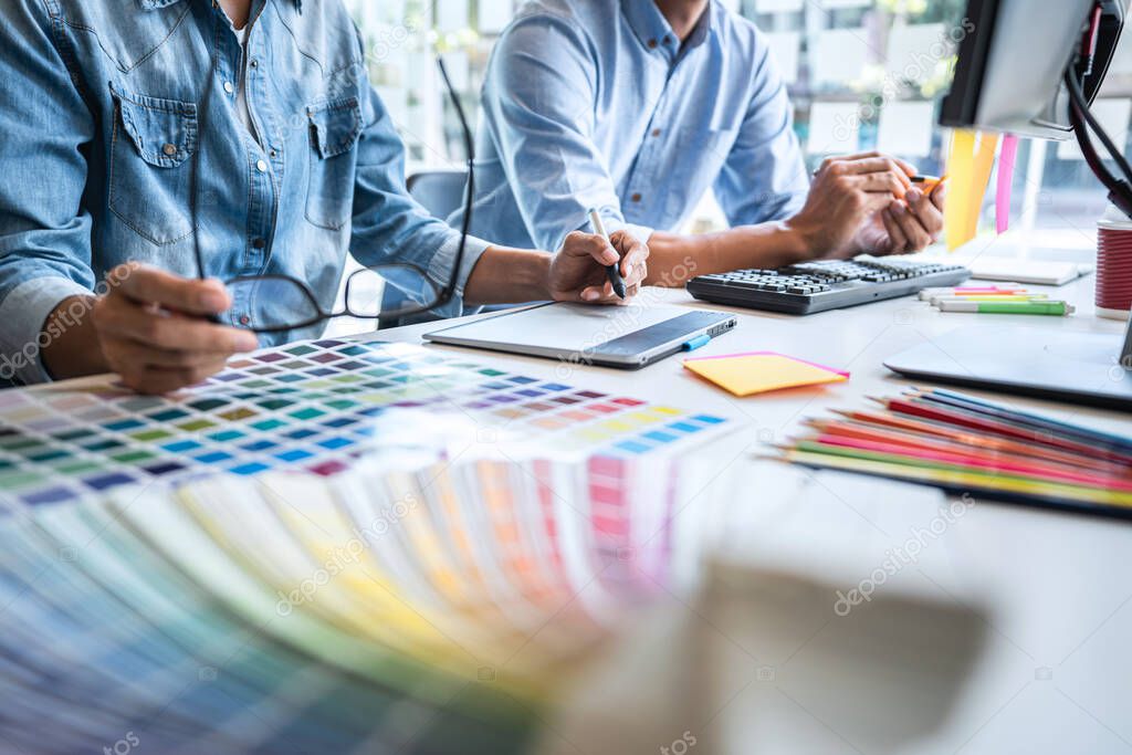 Two colleague creative graphic designer working on color selection and color swatches, drawing on graphics tablet at workplace with work tools and accessories.