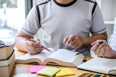 Eğitim, öğretim, öğrenme konsepti. Lise öğrencileri ya da sınıf arkadaşları kütüphanede ders çalışıp birlikte okuyorlar. Arkadaşların ödevlerini yapmasına ve giriş sınavına hazırlanmasına yardımcı oluyorlar..