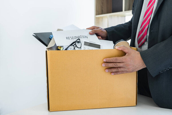 Businessman carrying packing up all his personal belongings and files into a brown cardboard box to resignation in modern office, resign concept.