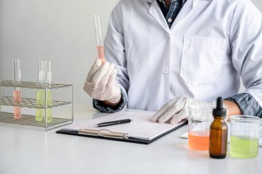 Laboratuvar önlüğündeki bilim adamı ya da tıp laboratuvar önlüğündeki deney tüpünü reaktörle tutarak cam şişede reaksiyonları karıştırarak kimyasal sıvı, laboratuvar araştırmaları ve testler içeren cam kaplar oluşturuyorlar..