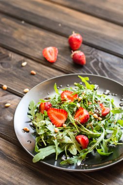 Taze salata roka ve Balsamik Sos ve çam fıstığı ile strawbery. Vejetaryen yiyecekler. Çilek salatası. Vitamini yiyecek, diyet salata ahşap arka planda siyah plaka üzerinde.