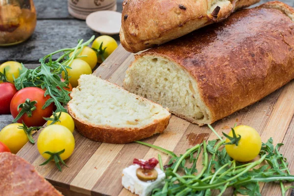 Fresh bread on wooden ground. Yellow tomato and red tomatoes with arugula. Feta cheese with olives and sundried tomatoes. Picnic, dinner outdoor. Still life of food. — Stock Photo, Image