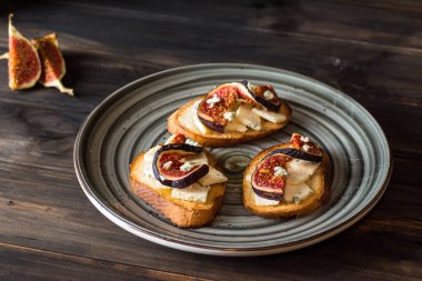 Ricotta, taze incir, ceviz ve bal siyah zemin üzerinde rustik ahşap tahta üzerinde sandviçle görünümü top. Bruschetta incir ile. Aperitive. Akdeniz mutfağı. Crostini.