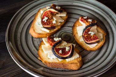 Ricotta, taze incir, ceviz ve bal siyah zemin üzerinde rustik ahşap tahta üzerinde sandviçle görünümü top. Bruschetta incir ile. Aperitive. Akdeniz mutfağı. Crostini.