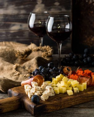 Ahşap tahta plaka üzerinde çeşitli peynirler. Camembert peyniri, peynir kabuğu meşe, sert peynir dilimleri, ceviz, üzüm, ekmek, kekik, üstten görünüm rendesi. Peynir ve şarap. Meze. Kırmızı şarap.