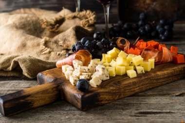 Ahşap tahta plaka üzerinde çeşitli peynirler. Camembert peyniri, peynir kabuğu meşe, sert peynir dilimleri, ceviz, üzüm, ekmek, kekik, üstten görünüm rendesi. Peynir ve şarap. Meze. Kırmızı şarap.