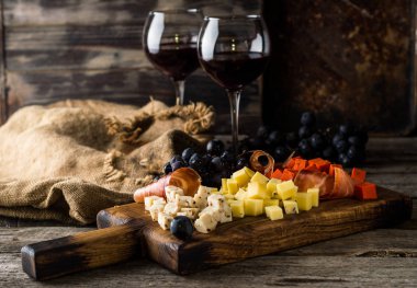 Ahşap tahta plaka üzerinde çeşitli peynirler. Camembert peyniri, peynir kabuğu meşe, sert peynir dilimleri, ceviz, üzüm, ekmek, kekik, üstten görünüm rendesi. Peynir ve şarap. Meze. Kırmızı şarap.