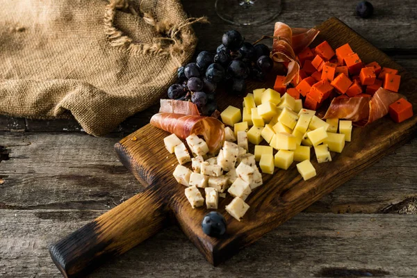 Fromages assortis sur plaque de bois. Fromage camembert, écorce râpée de chêne, tranches de fromage à pâte dure, noix, raisins, pain, thym, vue de dessus. Fromage et vin. Un antipasto. Vin rouge — Photo