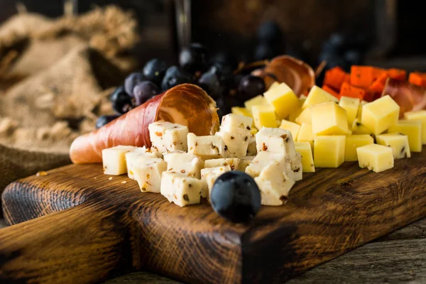 Queijos variados em placa de madeira. Queijo de camembert, casca ralada de carvalho, fatias de queijo duro, nozes, uvas, pão, tomilho, vista superior. Queijo e vinho. Antipasto. Vinho tinto — Fotografia de Stock