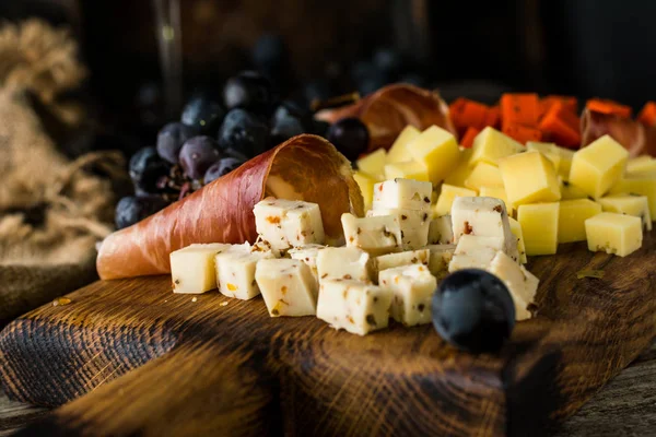 Queijos variados em placa de madeira. Queijo de camembert, casca ralada de carvalho, fatias de queijo duro, nozes, uvas, pão, tomilho, vista superior. Queijo e vinho. Antipasto. Vinho tinto — Fotografia de Stock