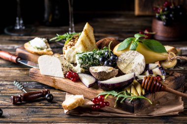 Peynir mezesi seçimi. Kırmızı frenk üzümü, bal, fesleğen, üzüm ve fındık ahşap beton zemin üzerinde rustik ahşap tahta, üst görünümü. Belper Knolle, keçi peyniri, Scamorza. Peynir tahtası, peynir tabağı