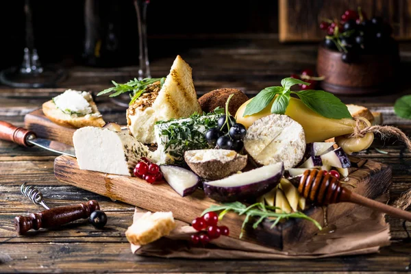 Selecção de aperitivos de queijo. Groselha vermelha, mel, manjericão, uvas e nozes em tábua de madeira rústica sobre fundo de concreto de madeira, vista superior. Belper Knolle, queijo de cabra, Scamorza. Tabuleiro de queijo, prato de queijo — Fotografia de Stock