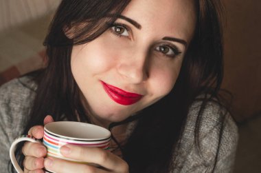 Genç güzel kadın bir fincan çay sıcak kazak rahat doğal ışık portre içinde tutar.