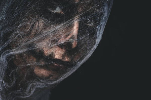 Жуткий персонаж, покрытый паутиной на черном фоне. Портрет жуткого существа Хэллоуина с копировальным пространством
