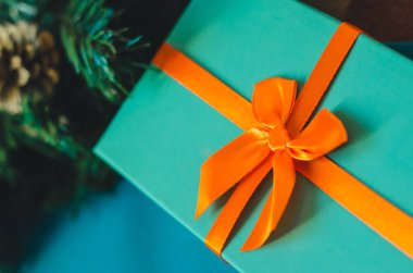 Turuncu bir yay ile masmavi hediye kutusu kadar yakın ve Noel ağacı dalı arka planda yeşil