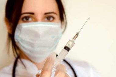 Genç kadın doktor stetoskop ve maske ile şırınga tutar ve kopya alanı yakın enjeksiyon için hazır
