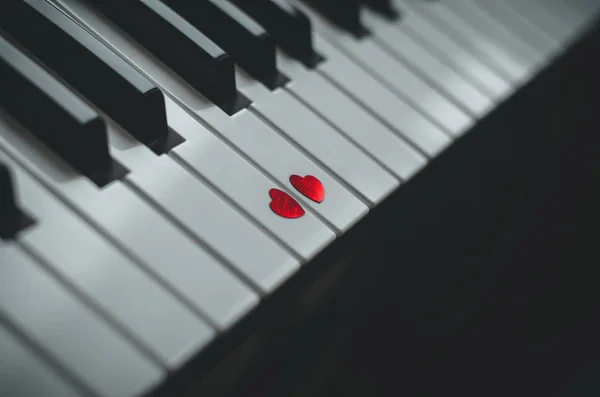 Two small red hearts on the white black keyboard of classic piano close up. Concept of love and romantic music. Copy space