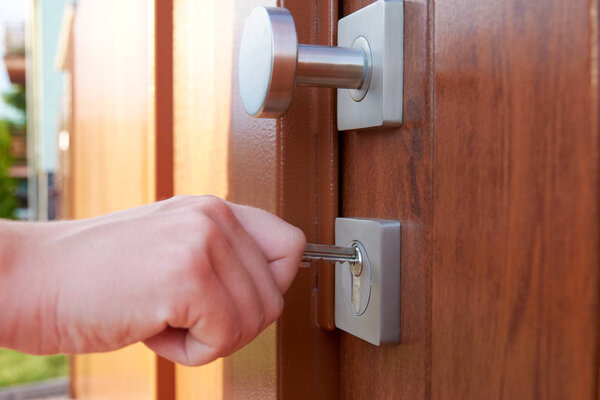 The young woman's hand holds the key and unlocks the lock on the door, outside