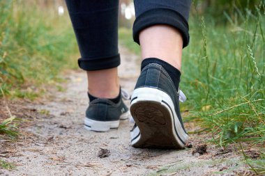 Genç kadın spor ayakkabı, kot bir yol çimen, bir orman içinde bir yaz veya bahar gününde yürürken