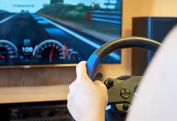 Young woman playing a racing game on a gaming console holding a steering wheel and driving a car on a television screen