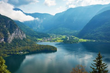 Şehir ve Avusturya'da, Hallstatt Gölü Alps dağlar bulutlar ve orman içinde belgili tanımlık geçmiş bir aydınlık ve güneşli gün ile mavi gökyüzü altında görünümü