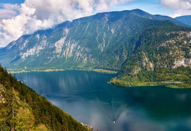 Şehir ve Avusturya'da, Hallstatt Gölü Alps dağlar bulutlar ve orman içinde belgili tanımlık geçmiş bir aydınlık ve güneşli gün ile mavi gökyüzü altında görünümü