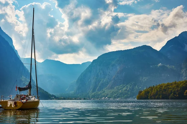 A view of Lake Hallstatt with a yacht and mountains with a forest in the background, under a blue sky with dramatic clouds. Austria in Europe