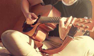 Genç kadın bir akustik gitar çalmak yatakta oturuyordu. Yaz günü sabahı güneş.