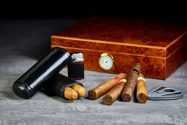 Six Cuban cigars on a stone table with a lighter, cutter and a wooden humidor. Leather case.