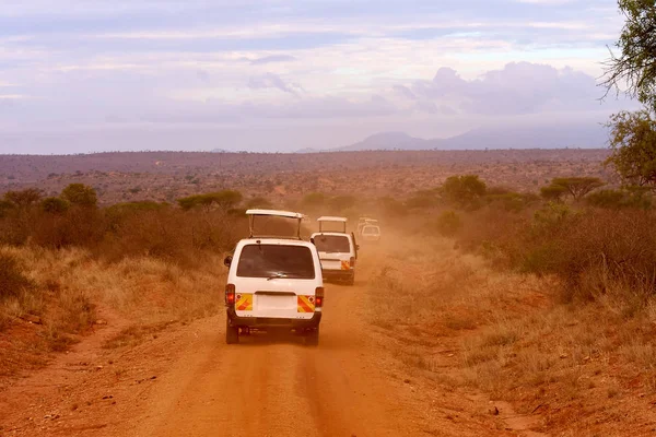Several safari cars in Kenya in Africa, red sand and mountains in the background